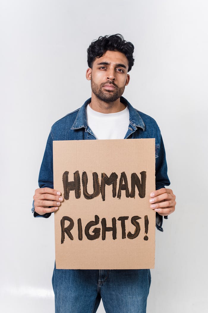 A young man holds a cardboard sign advocating for human rights indoors.