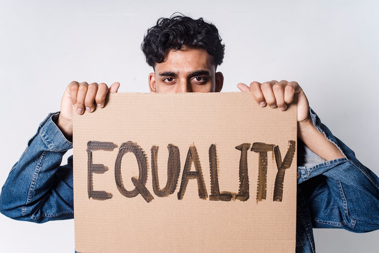 A man holds a cardboard sign reading 'EQUALITY' in a studio.